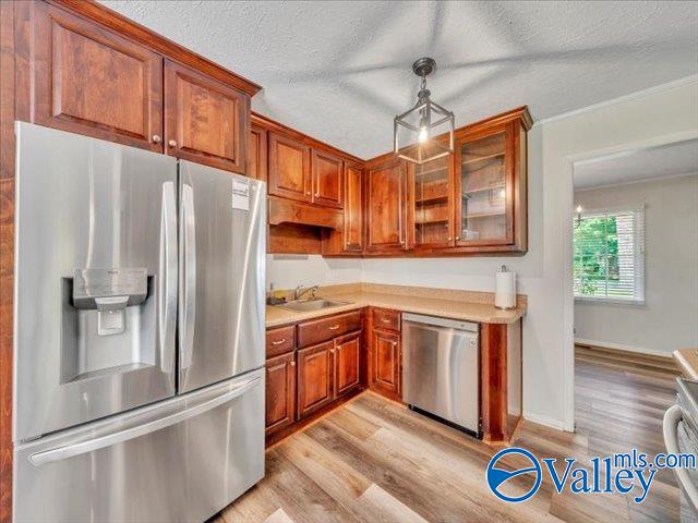 kitchen with stainless steel appliances, light wood-type flooring, light countertops, glass insert cabinets, and a textured ceiling