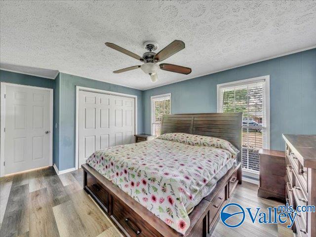 bedroom featuring multiple windows, wood finished floors, a closet, a ceiling fan, and a textured ceiling