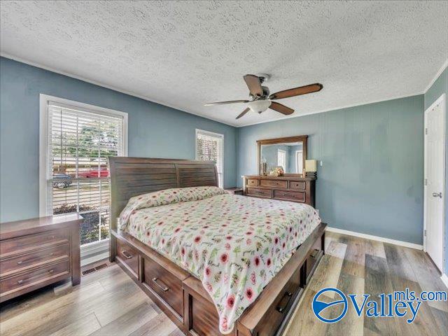 bedroom with light wood-type flooring, multiple windows, a textured ceiling, and a ceiling fan