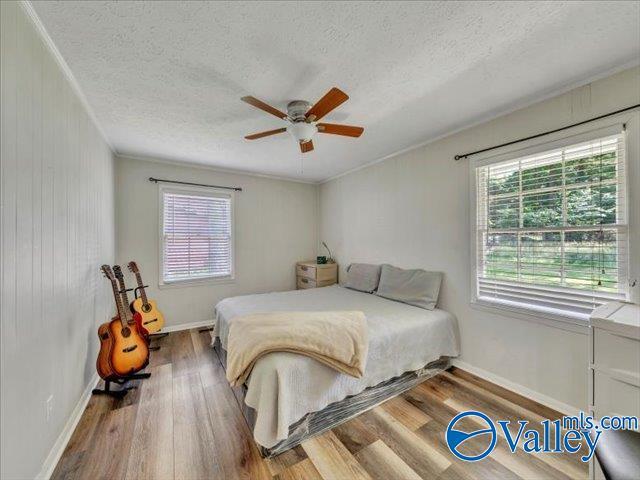 bedroom with multiple windows, a textured ceiling, wood finished floors, baseboards, and ornamental molding