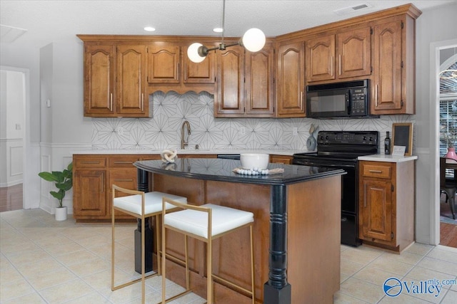 kitchen featuring a breakfast bar area, light tile patterned floors, a kitchen island, and black appliances