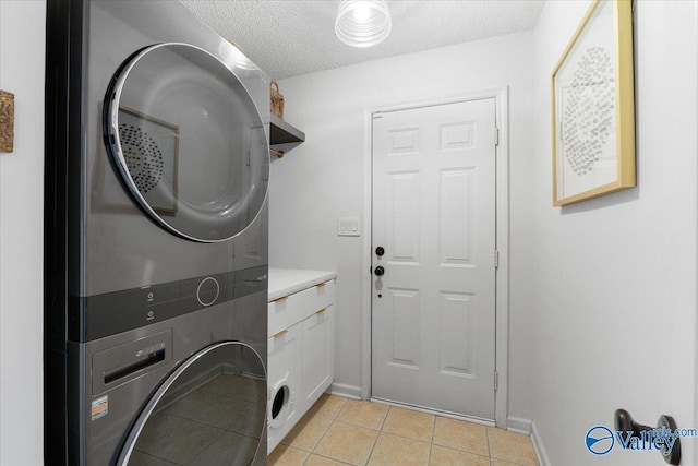 washroom with light tile patterned floors, cabinets, a textured ceiling, and stacked washing maching and dryer