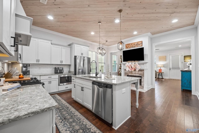 kitchen with decorative light fixtures, an island with sink, white cabinets, light stone counters, and stainless steel appliances