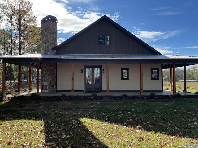 farmhouse inspired home with a front yard, a chimney, french doors, board and batten siding, and metal roof