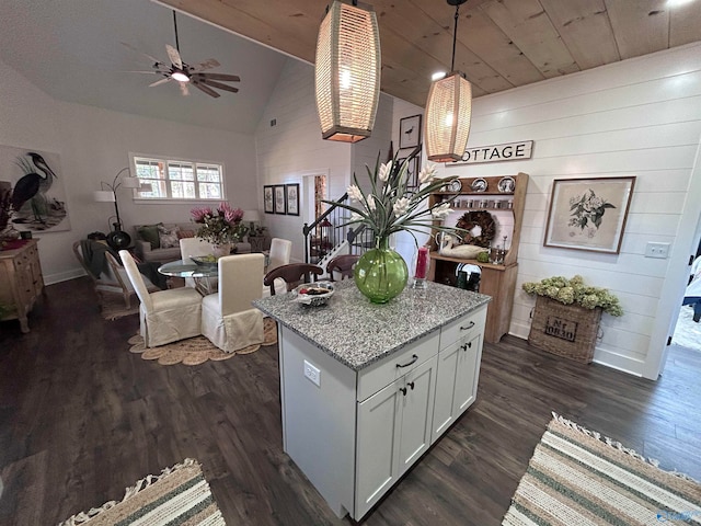 kitchen with a center island, white cabinets, hanging light fixtures, light stone counters, and dark hardwood / wood-style flooring