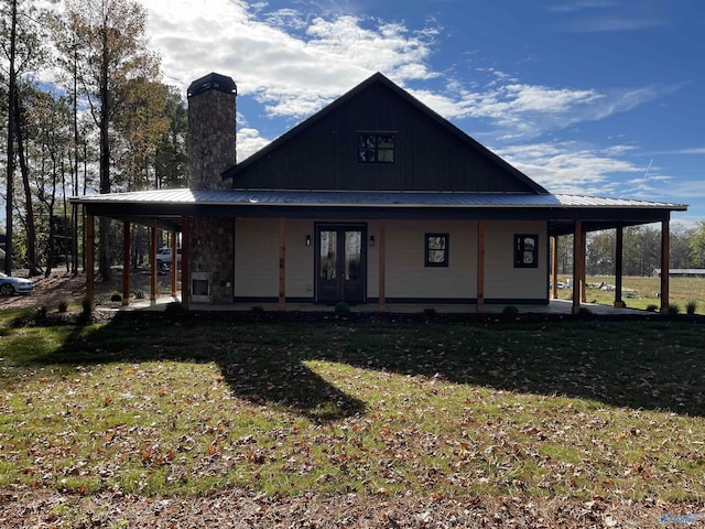 back of property featuring a lawn, french doors, metal roof, a carport, and a chimney