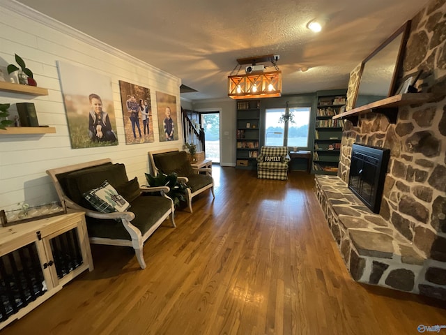 living room featuring a stone fireplace, wood-type flooring, ornamental molding, and a textured ceiling