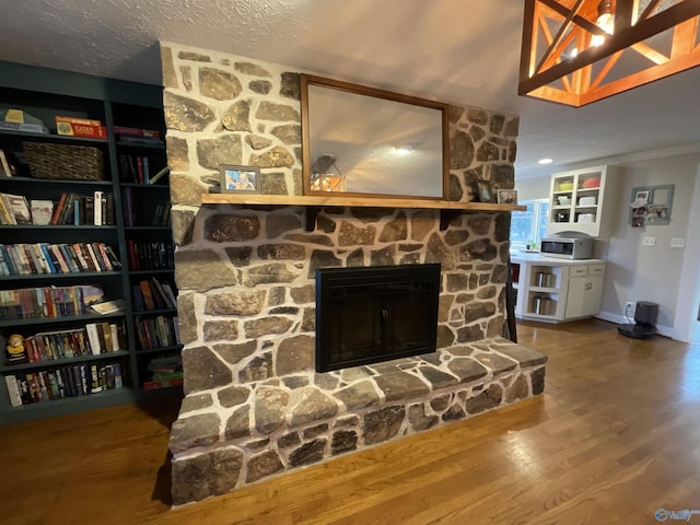 living room with crown molding, a stone fireplace, and hardwood / wood-style flooring