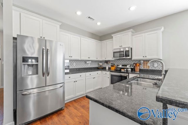 kitchen featuring white cabinetry, wood-type flooring, sink, decorative backsplash, and stainless steel appliances