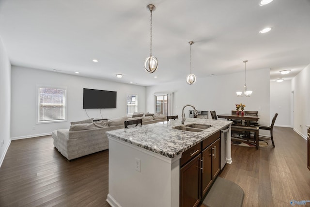 kitchen with dark wood-style floors, pendant lighting, light stone counters, and a sink