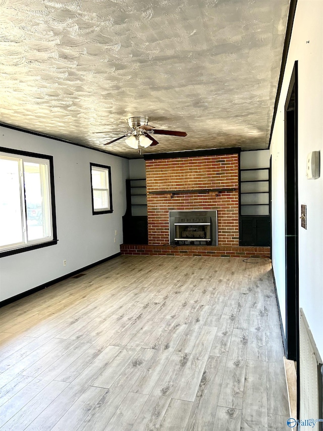 unfurnished living room featuring ceiling fan, light wood-type flooring, and a brick fireplace