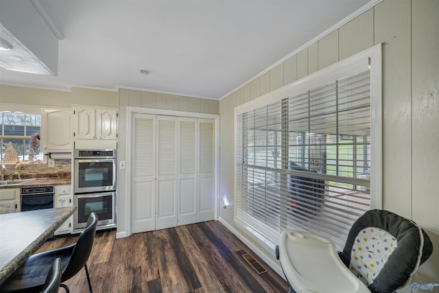 kitchen with dark hardwood / wood-style flooring, double oven, crown molding, wooden walls, and white cabinets