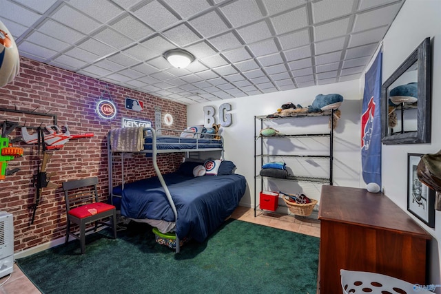 bedroom featuring tile patterned floors, a drop ceiling, and brick wall