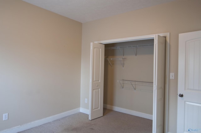 unfurnished bedroom featuring baseboards, a closet, and light colored carpet