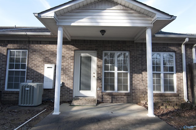 doorway to property featuring brick siding, a patio, and central air condition unit