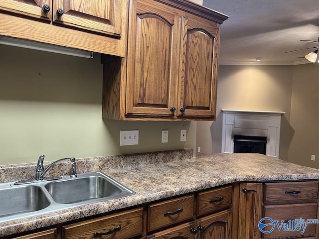 kitchen featuring crown molding, a fireplace, light countertops, a sink, and ceiling fan