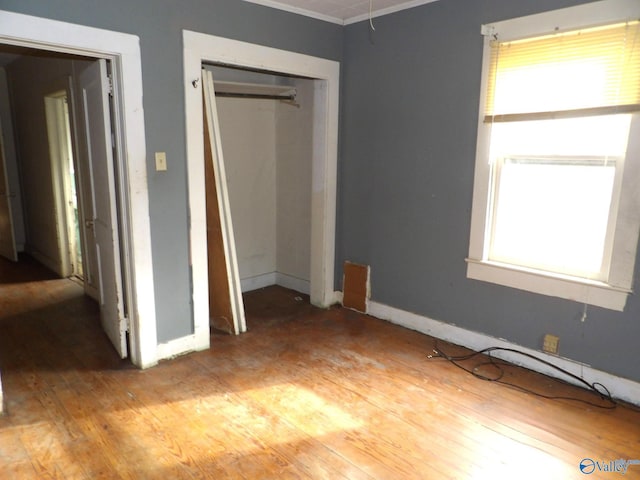 unfurnished bedroom featuring ornamental molding, a closet, light wood-style flooring, and baseboards