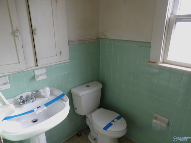 bathroom with a sink, tile walls, and toilet