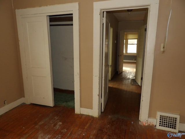 hallway with wood-type flooring, visible vents, and baseboards