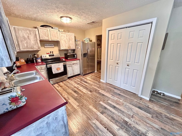 kitchen featuring stainless steel appliances, a textured ceiling, light brown cabinets, sink, and light hardwood / wood-style floors