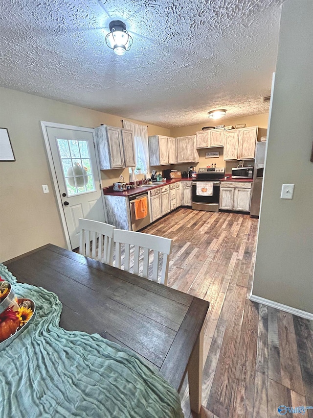 kitchen with wood-type flooring, appliances with stainless steel finishes, a textured ceiling, light brown cabinets, and sink