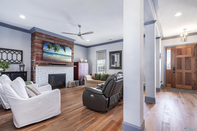 living room featuring a tiled fireplace, ornamental molding, hardwood / wood-style floors, and ceiling fan