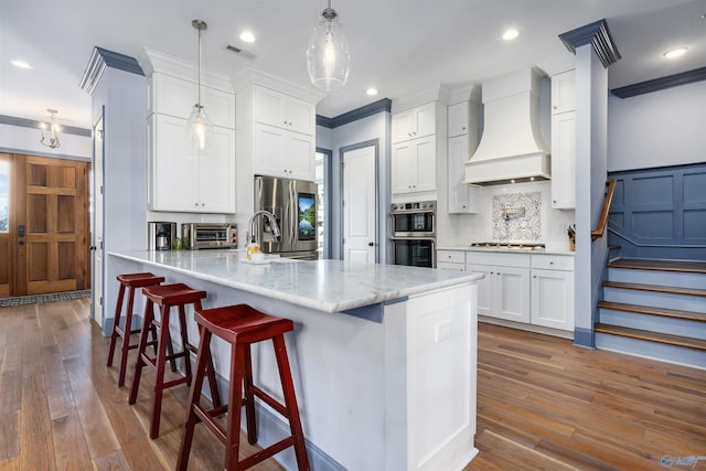 kitchen with custom exhaust hood, white cabinets, pendant lighting, stainless steel appliances, and backsplash