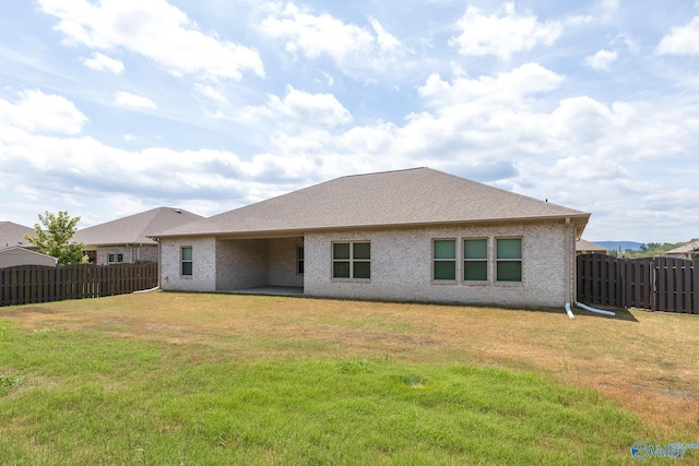 rear view of house with a fenced backyard, brick siding, and a yard