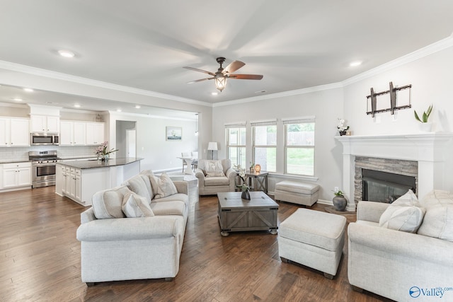 living area featuring baseboards, dark wood finished floors, ornamental molding, a stone fireplace, and ceiling fan