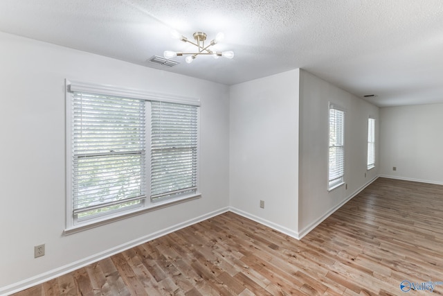 unfurnished room featuring an inviting chandelier, a textured ceiling, wood-type flooring, and a wealth of natural light