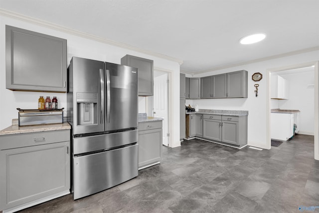 kitchen featuring light stone counters, stainless steel fridge, gray cabinets, and crown molding