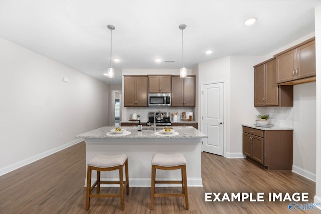 122 Burdine St, New Market, AL 35761 - kitchen featuring a kitchen island with sink, decorative light fixtures, stainless steel microwave, decorative backsplash, and baseboards