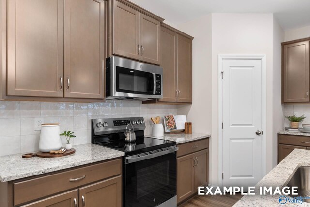 122 Burdine St, New Market, AL 35761 - kitchen with appliances with stainless steel finishes, tasteful backsplash, light stone counters, and wood finished floors