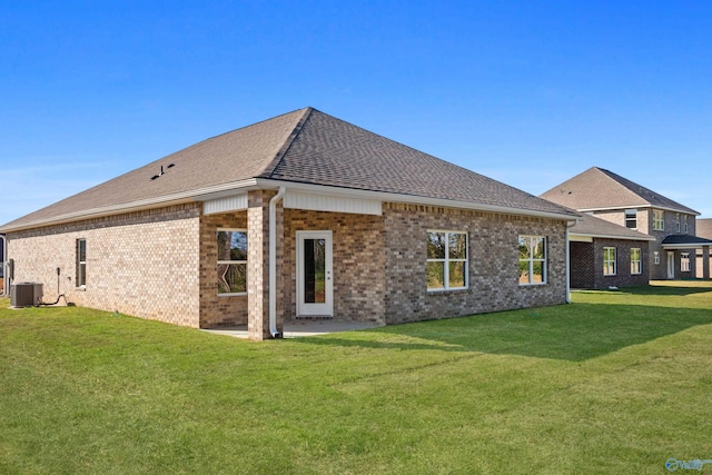 back of property with a shingled roof, brick siding, a lawn, and central air condition unit