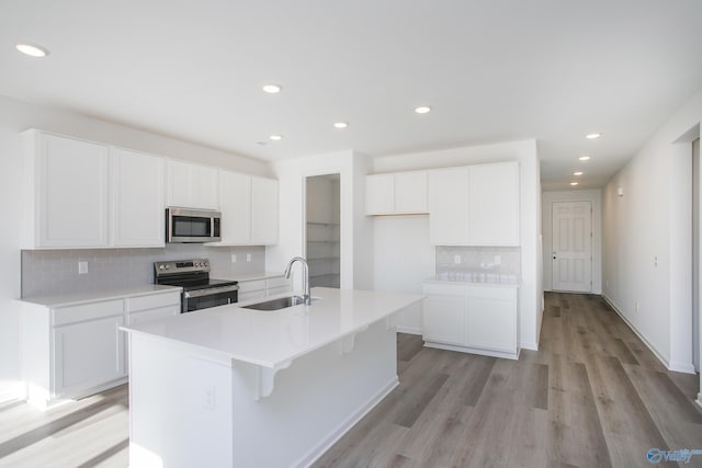 kitchen featuring light hardwood / wood-style flooring, sink, stainless steel appliances, white cabinets, and an island with sink