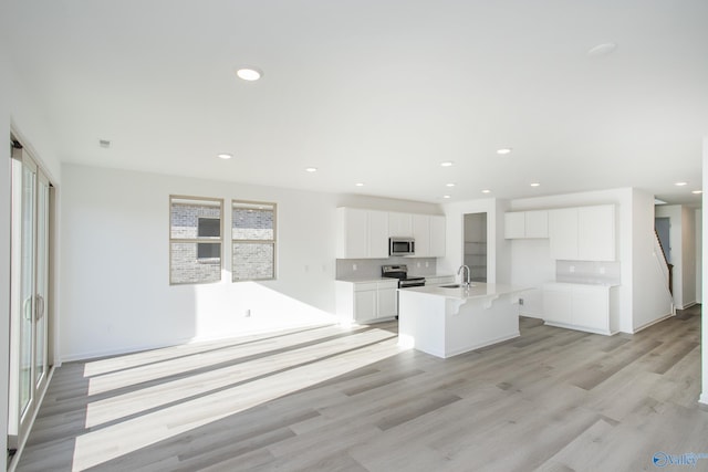 kitchen featuring white cabinetry, a center island with sink, stainless steel appliances, light hardwood / wood-style flooring, and sink