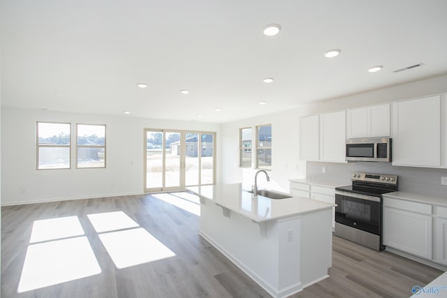 kitchen featuring a center island with sink, appliances with stainless steel finishes, sink, light hardwood / wood-style floors, and white cabinets