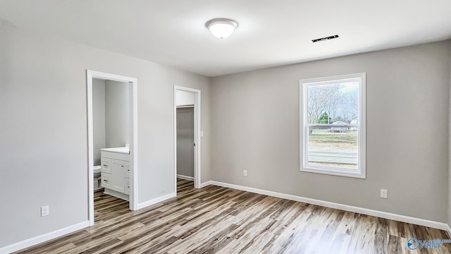 unfurnished bedroom featuring light wood-type flooring, a walk in closet, ensuite bath, and a closet