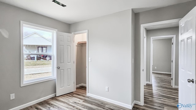 unfurnished bedroom featuring a walk in closet, a closet, light hardwood / wood-style flooring, and multiple windows