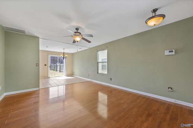 spare room featuring visible vents, baseboards, wood finished floors, and ceiling fan with notable chandelier