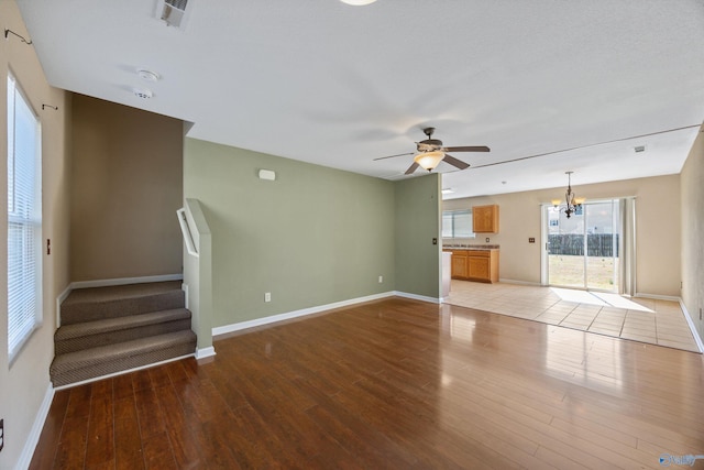 unfurnished living room with visible vents, baseboards, light wood-style floors, and ceiling fan with notable chandelier