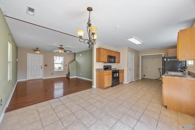 kitchen with black appliances, ceiling fan with notable chandelier, a sink, open floor plan, and light tile patterned floors