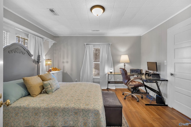 bedroom with wood finished floors, visible vents, and ornamental molding