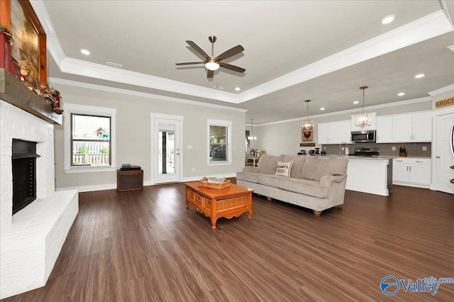 living room with dark hardwood / wood-style floors, ceiling fan, a raised ceiling, and a fireplace