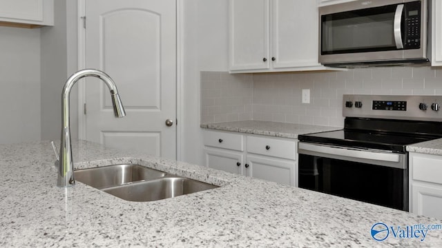 kitchen with sink, tasteful backsplash, stainless steel appliances, light stone countertops, and white cabinets