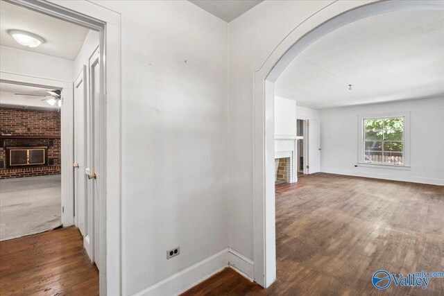 hall featuring wood finished floors, arched walkways, and baseboards