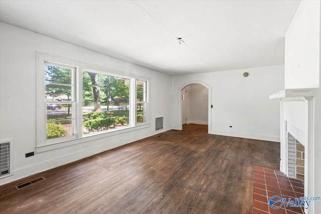 unfurnished living room featuring wood finished floors, a fireplace with flush hearth, arched walkways, and visible vents