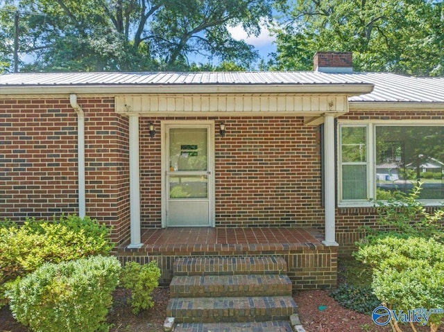 doorway to property with brick siding, a chimney, and metal roof