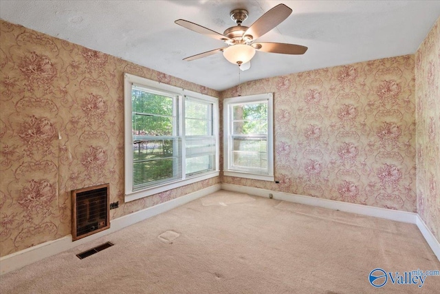 unfurnished living room featuring visible vents, wallpapered walls, carpet floors, heating unit, and a ceiling fan