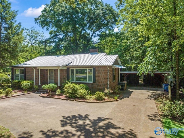 single story home featuring metal roof, brick siding, driveway, and a chimney